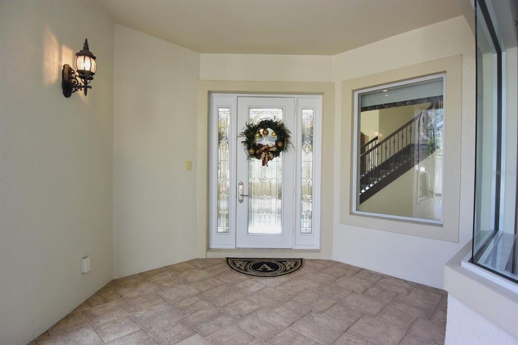 A covered entryway features a tiled floor, a decorative front door, and a wall-mounted lantern — 285 WOODSTREAM WAY, SPRING HILL, FL