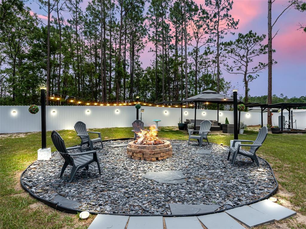 A backyard fire pit area features a stone fire ring, Adirondack chairs, and string lighting — 15255 SW 50TH AVENUE ROAD, OCALA, FL