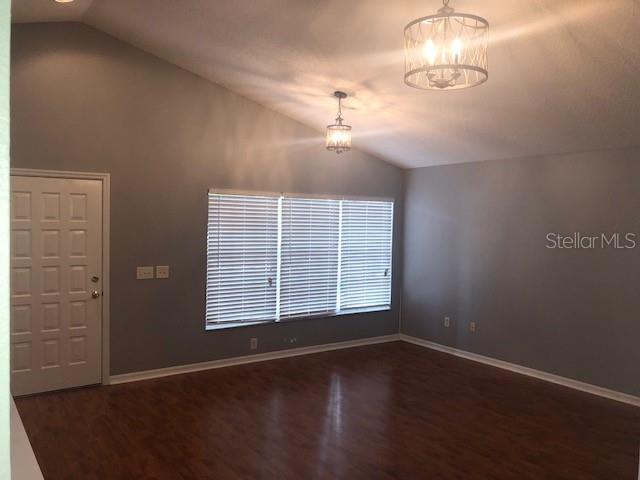 An empty room features gray walls, wood-look flooring, a vaulted ceiling, and two hanging light fixtures — 1851 FALLING STAR LANE, LUTZ, FL