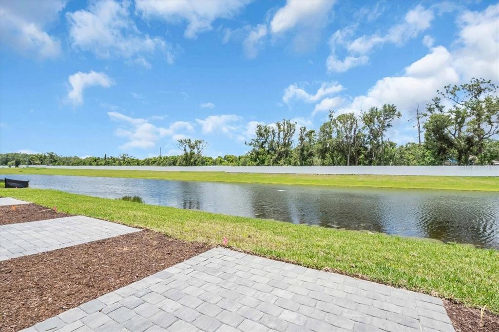 A paved patio overlooks a grassy lawn, a pond, and a line of trees — 14322 LILAC SKY TERRACE, BRADENTON, FL
