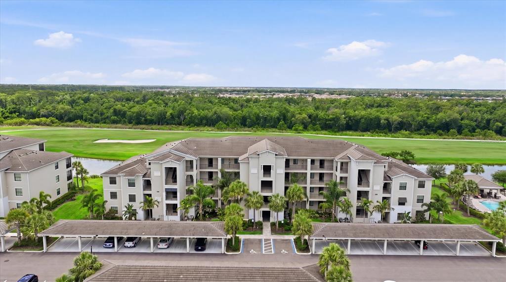 An aerial view shows a multi-story apartment building with covered parking in the foreground — 17810 GAWTHROP DRIVE UNIT 203, LAKEWOOD RANCH, FL