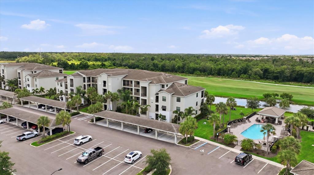 An aerial view shows a multi-story apartment building with covered parking and a swimming pool — 17810 GAWTHROP DRIVE UNIT 203, LAKEWOOD RANCH, FL
