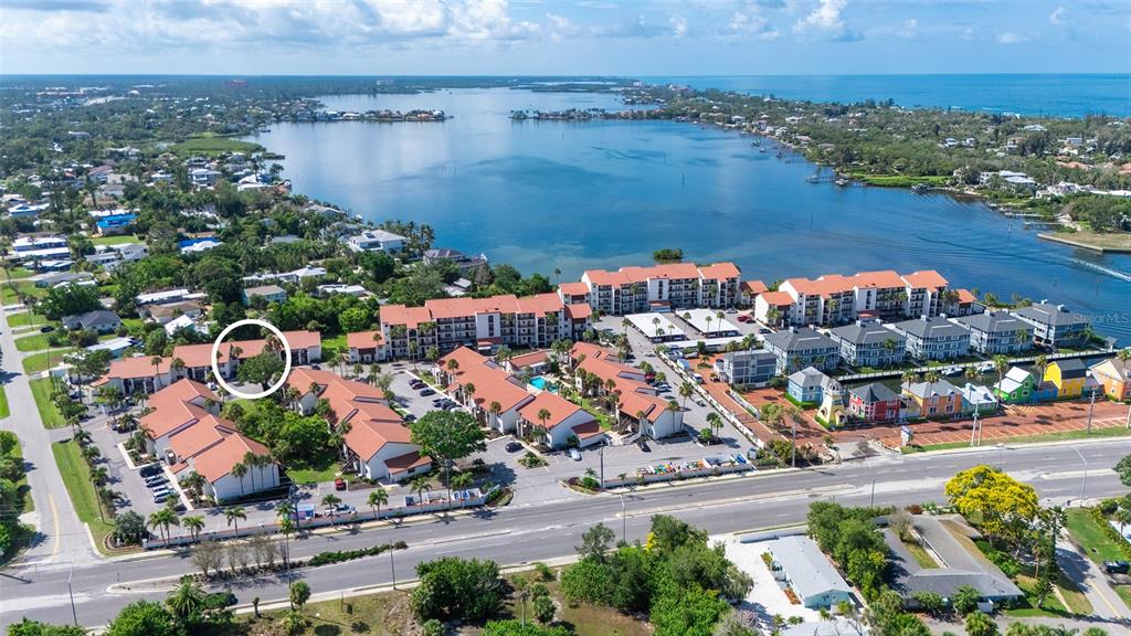An aerial view shows a residential complex with red-roofed buildings near a large body of water — 1646 STICKNEY POINT ROAD UNIT 101, SARASOTA, FL