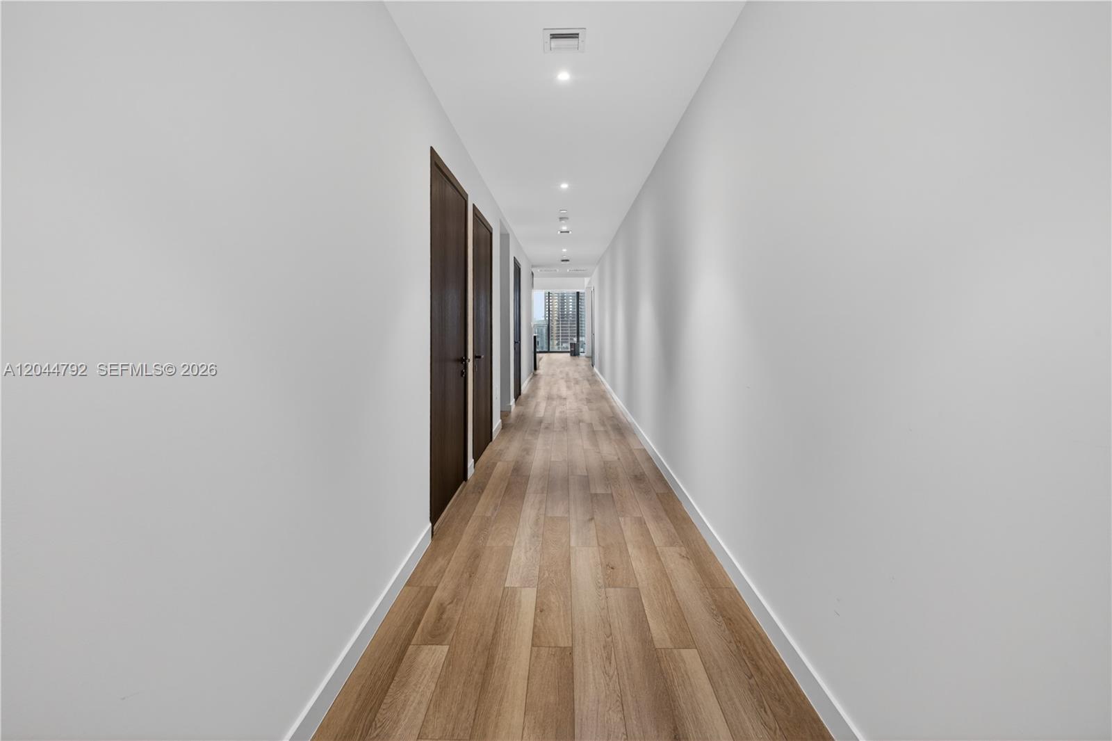 A long, narrow hallway features light wood flooring, white walls, and dark wooden doors — 20 NE 11th # 4703, Miami FL 33132, MIAMI, FL