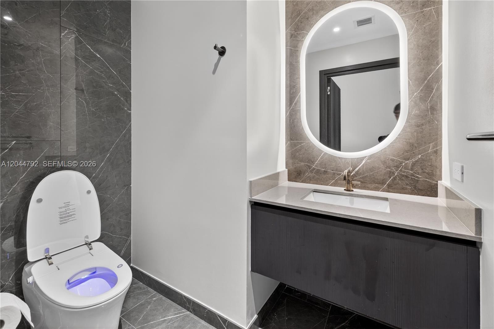 A modern bathroom features a floating vanity, a backlit oval mirror, and a smart toilet — 20 NE 11th # 4703, Miami FL 33132, MIAMI, FL
