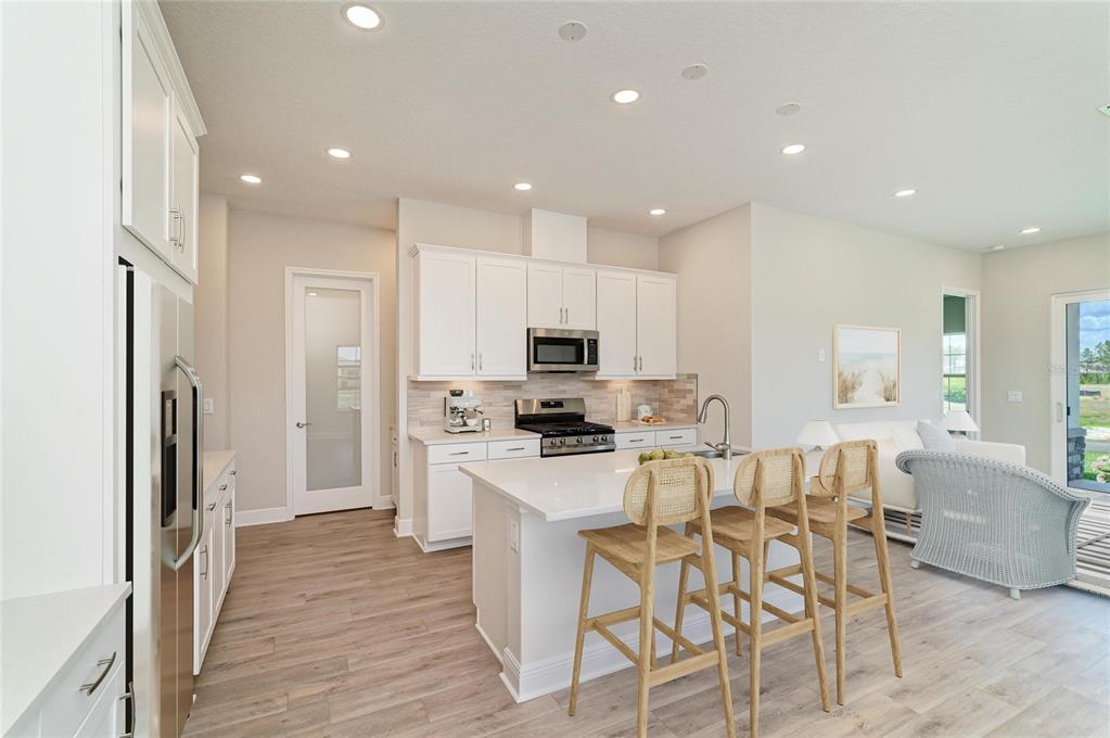 A bright kitchen features white cabinetry, a central island with bar stools, and light flooring — 35517 STABLETON LANE, ZEPHYRHILLS, FL