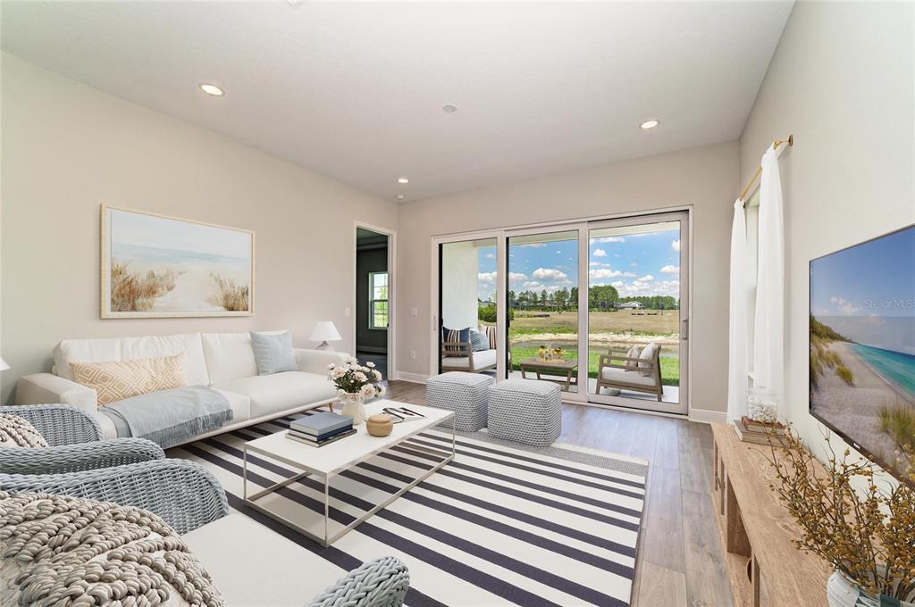 A living room features a white sofa, striped rug, and sliding glass doors overlooking a pond — 35517 STABLETON LANE, ZEPHYRHILLS, FL