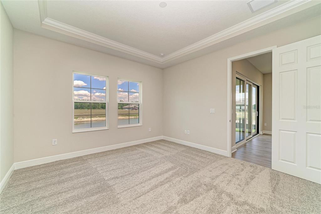 An empty bedroom with beige carpet, a tray ceiling, and a view of a pond — 35517 STABLETON LANE, ZEPHYRHILLS, FL
