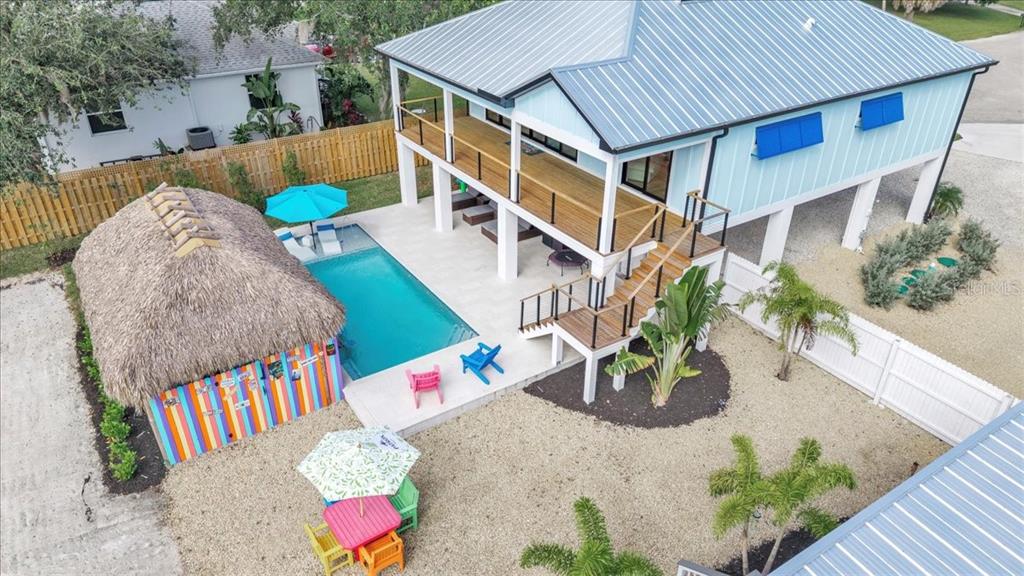 An elevated house with a metal roof, a swimming pool, and a thatched-roof tiki bar — 9470 COLONY DRIVE, NORTH FORT MYERS, FL