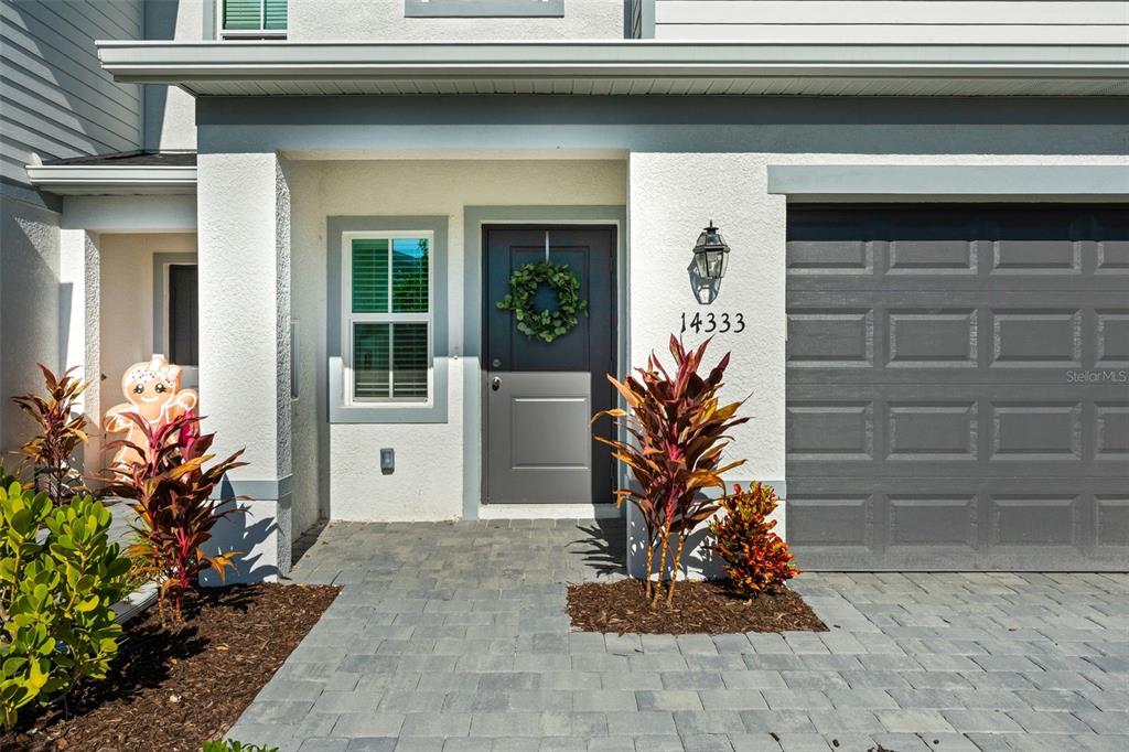 A paved walkway leads to the front entrance of a house with a gray door — 14333 LILAC SKY TERRACE, BRADENTON, FL