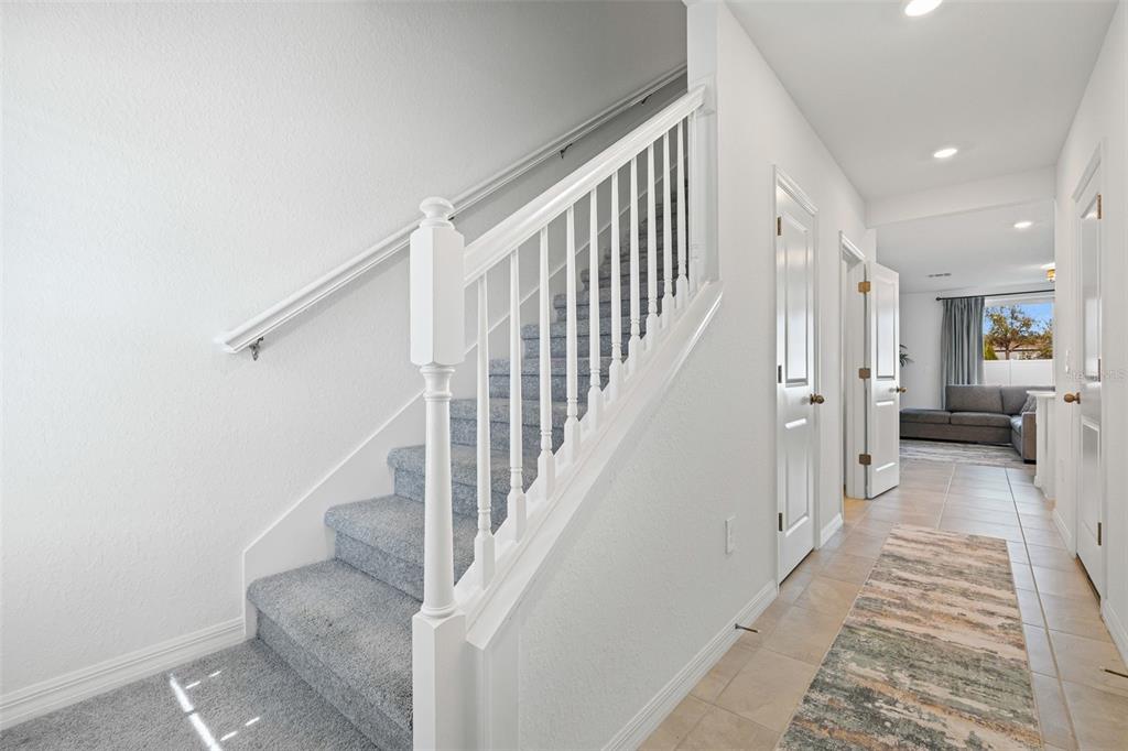 A carpeted staircase with a white railing sits beside a hallway with tiled floors — 14333 LILAC SKY TERRACE, BRADENTON, FL