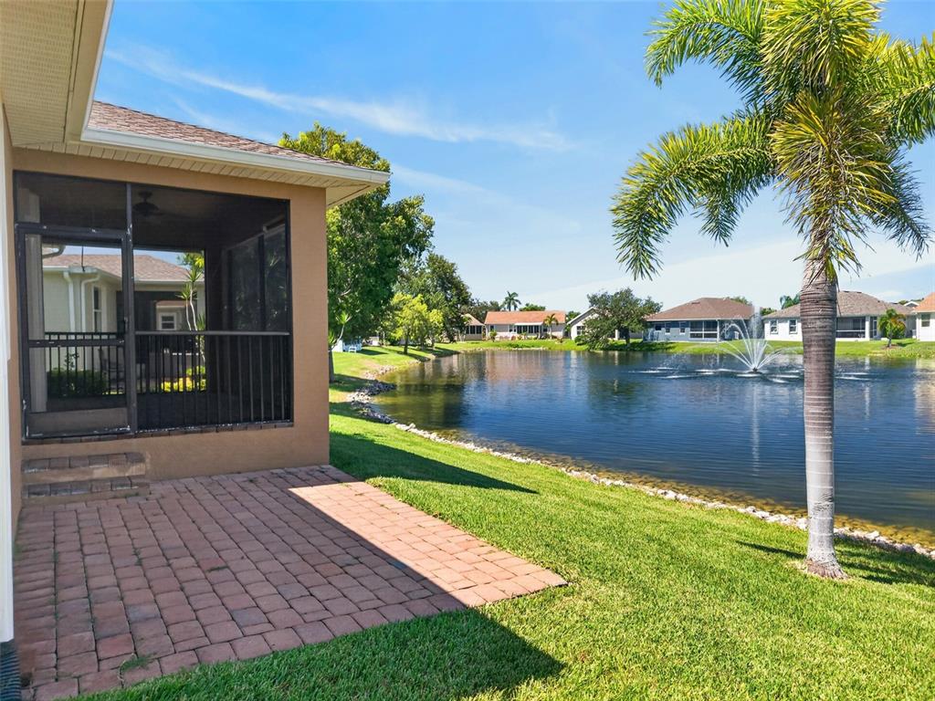 A paved patio sits beside a screened-in porch overlooking a pond with a fountain — 24803 RIO VILLA LAKES CIRCLE, PUNTA GORDA, FL
