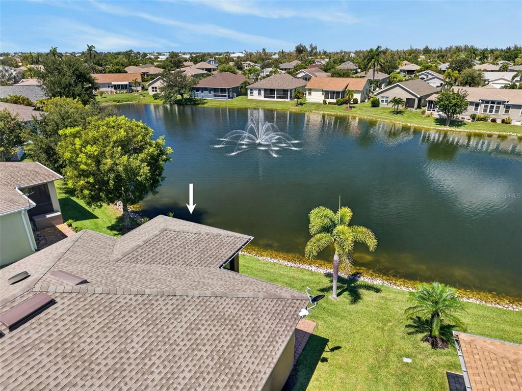 An aerial view shows a house roof overlooking a pond with a fountain and surrounding homes — 24803 RIO VILLA LAKES CIRCLE, PUNTA GORDA, FL