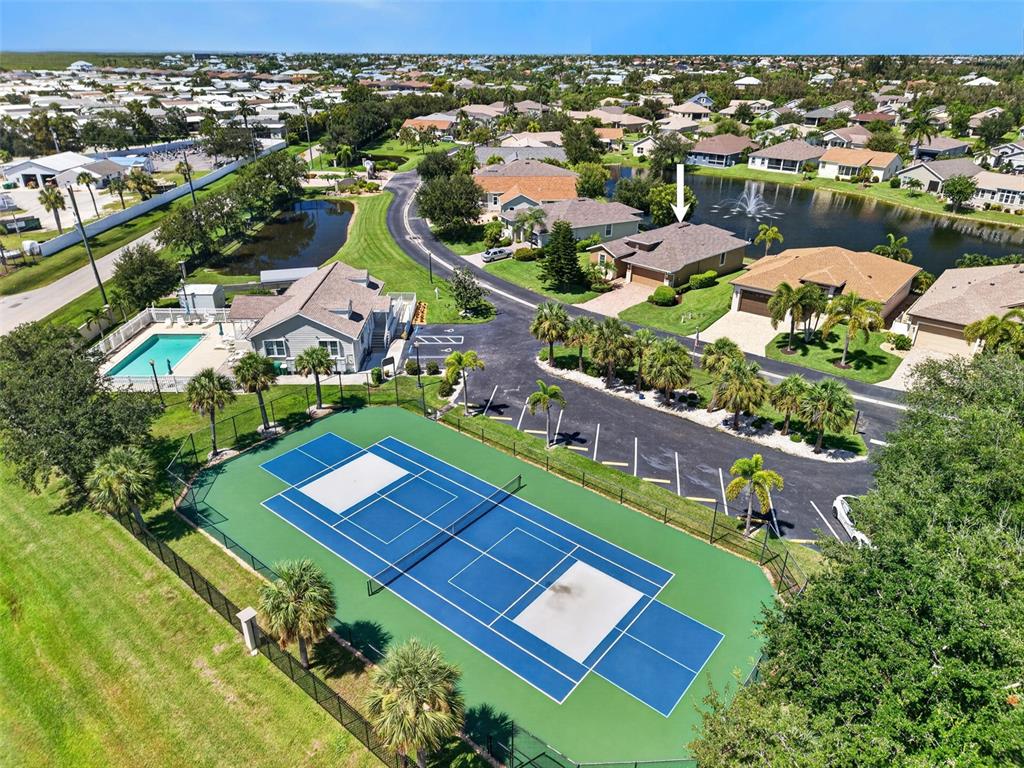 An aerial view shows a tennis court, a swimming pool, and residential houses near a lake — 24803 RIO VILLA LAKES CIRCLE, PUNTA GORDA, FL