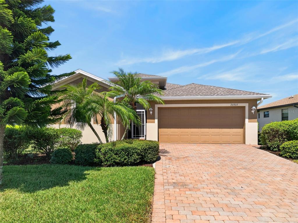 A single-story house with a tan stucco exterior, a two-car garage, and a brick driveway — 24803 RIO VILLA LAKES CIRCLE, PUNTA GORDA, FL