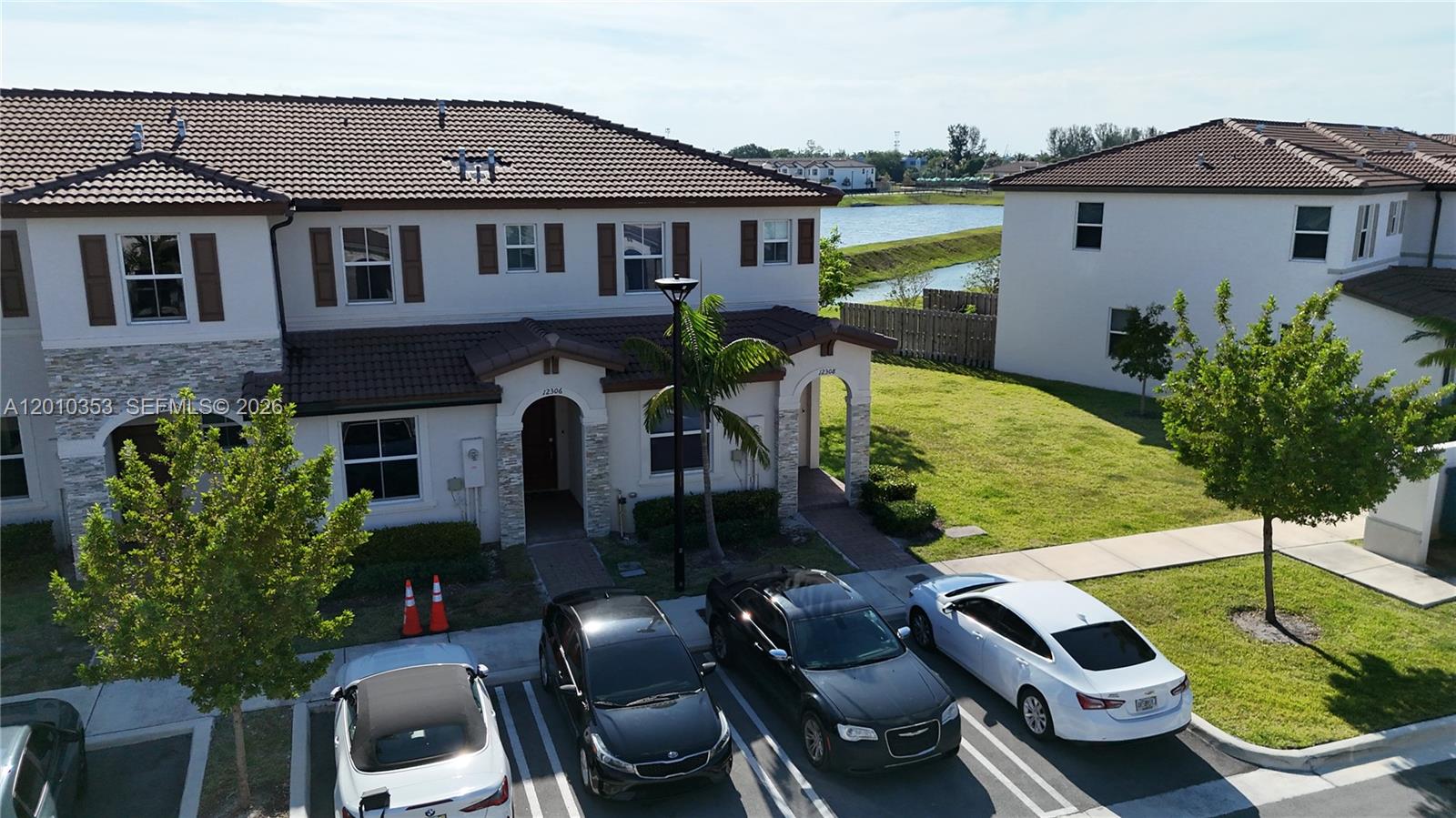 An aerial view shows two-story townhomes with tiled roofs, parking spaces, and a nearby pond — 12308 NW 23rd Ct # 12308, Miami FL 33167, MIAMI, FL
