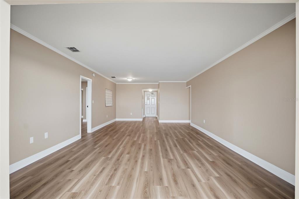 An empty room with light-colored walls, crown molding, and wood-look vinyl plank flooring — 5108 BRITTANY DRIVE S UNIT 1006, ST PETERSBURG, FL