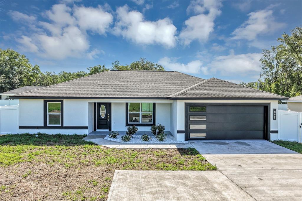 A single-story house with white stucco walls, black trim, and a dark garage door — 10449 SW 140TH AVENUE, DUNNELLON, FL