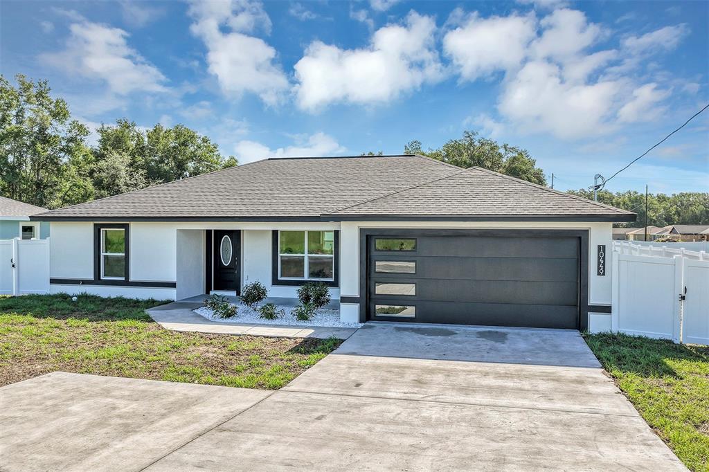 A single-story house features a white exterior, a dark garage door, and a concrete driveway — 10449 SW 140TH AVENUE, DUNNELLON, FL