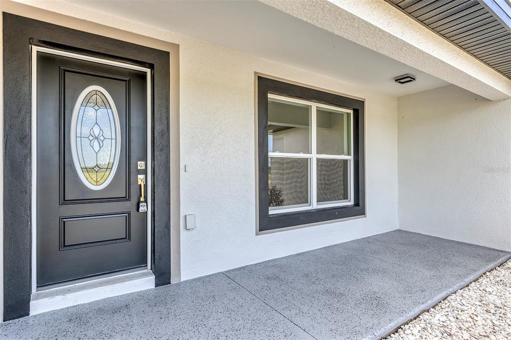 A front porch with a black door and window trim, white stucco walls, and speckled flooring — 10449 SW 140TH AVENUE, DUNNELLON, FL
