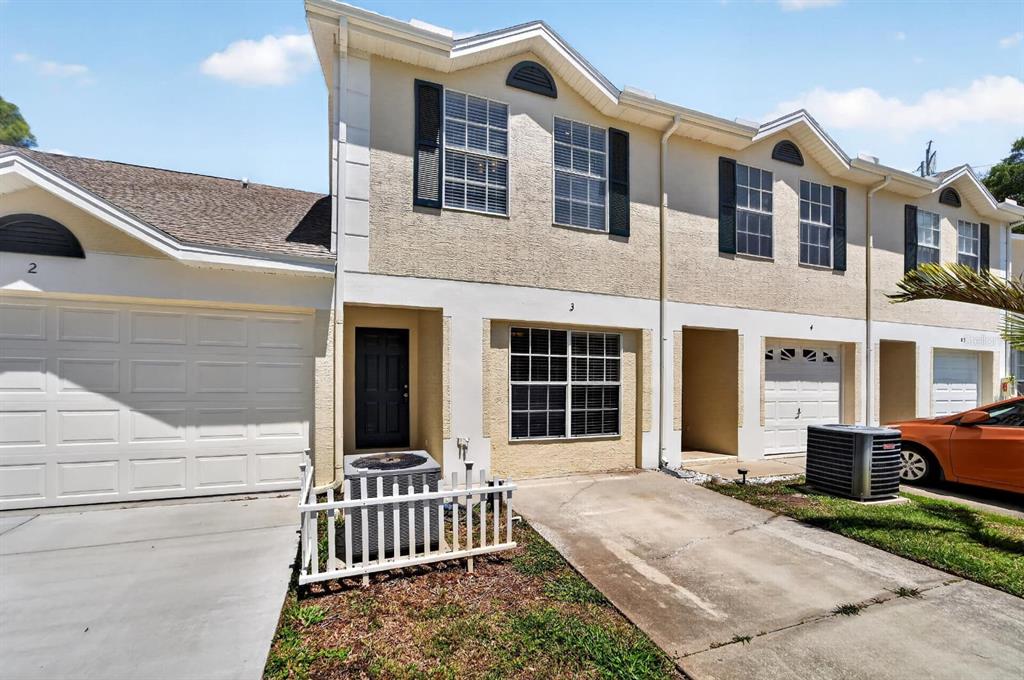 A row of two-story townhomes with beige stucco siding, dark shutters, and attached garages — 658 GREEN VALLEY ROAD UNIT B3, PALM HARBOR, FL