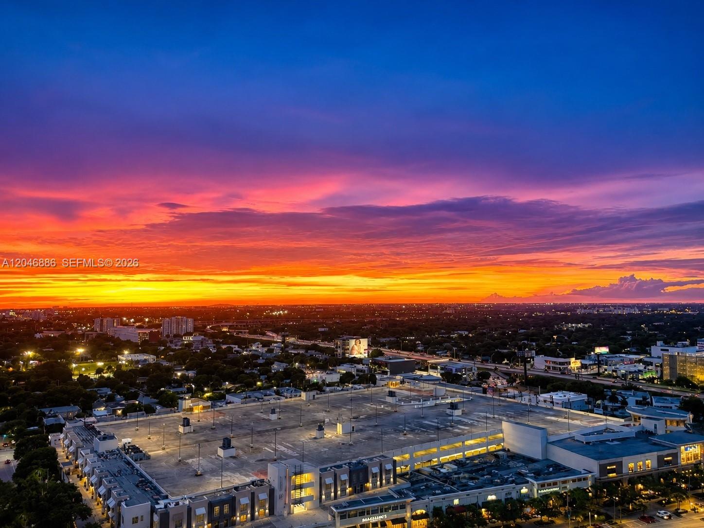 An aerial view shows a parking garage rooftop at sunset with a city skyline beyond — 3301 NE 1st Ave # H2113, Miami FL 33137, MIAMI, FL