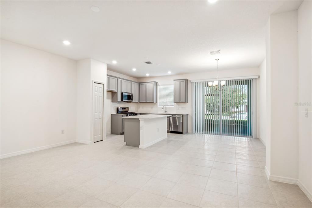 A kitchen with gray cabinets, a central island, and tile flooring opens to a dining area — 5756 SPOTTED HARRIER WAY, LITHIA, FL