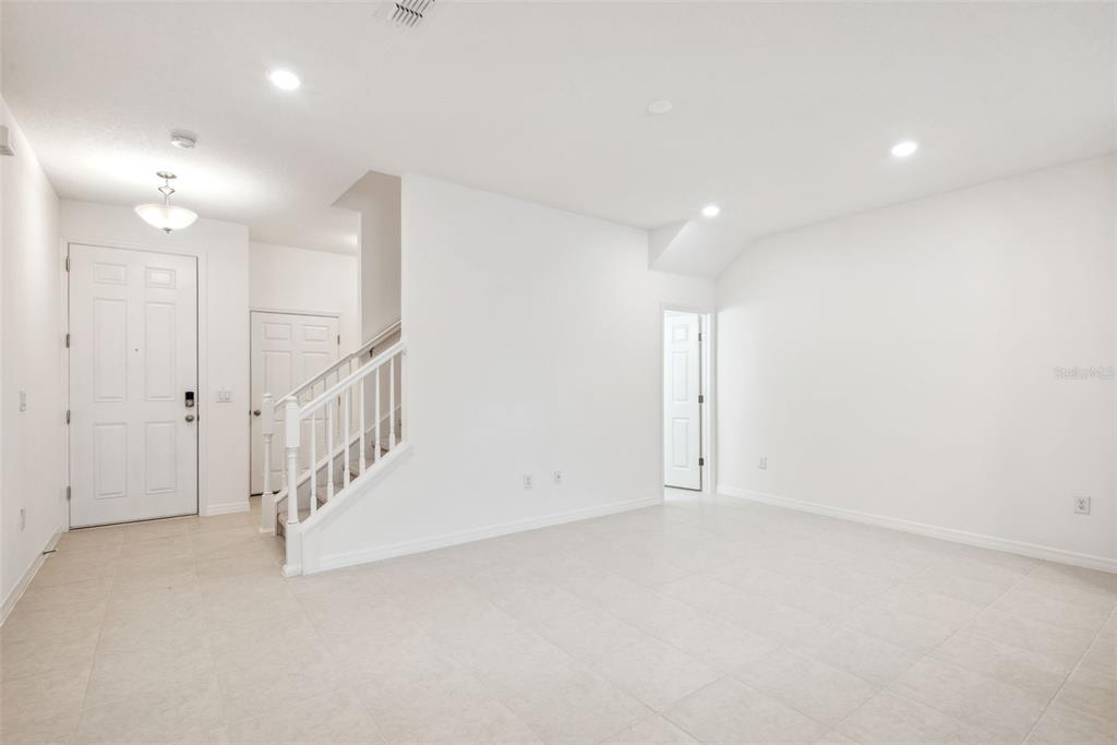 A bright, empty room with white walls, tile flooring, a staircase, and a front door — 5756 SPOTTED HARRIER WAY, LITHIA, FL