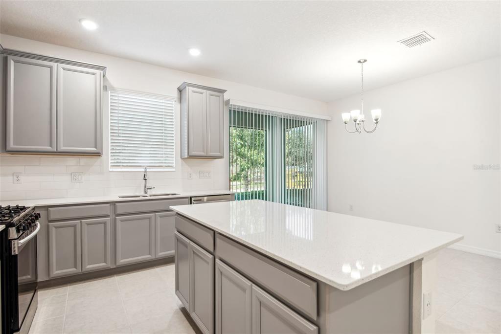 A kitchen with gray cabinets, white countertops, a center island, and a dining area — 5756 SPOTTED HARRIER WAY, LITHIA, FL