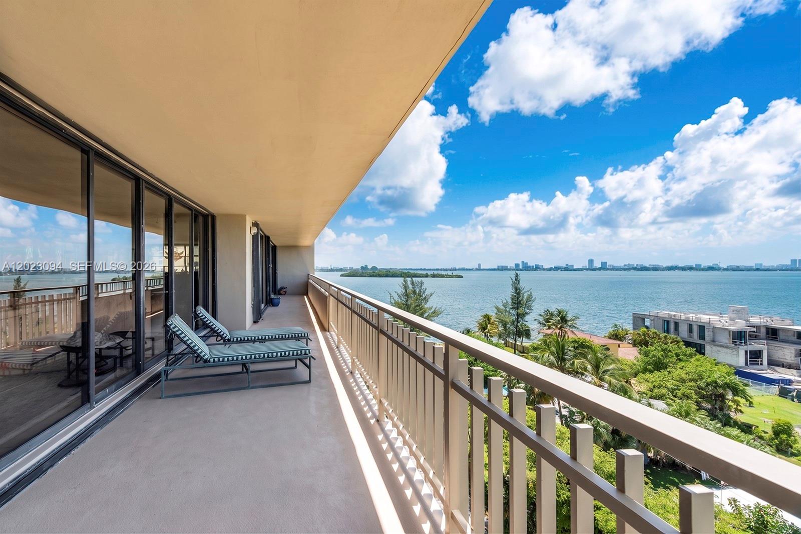 A balcony with lounge chairs overlooks a bay, trees, and a distant city skyline — 11113 Biscayne Blvd # 751, Miami FL 33181, MIAMI, FL