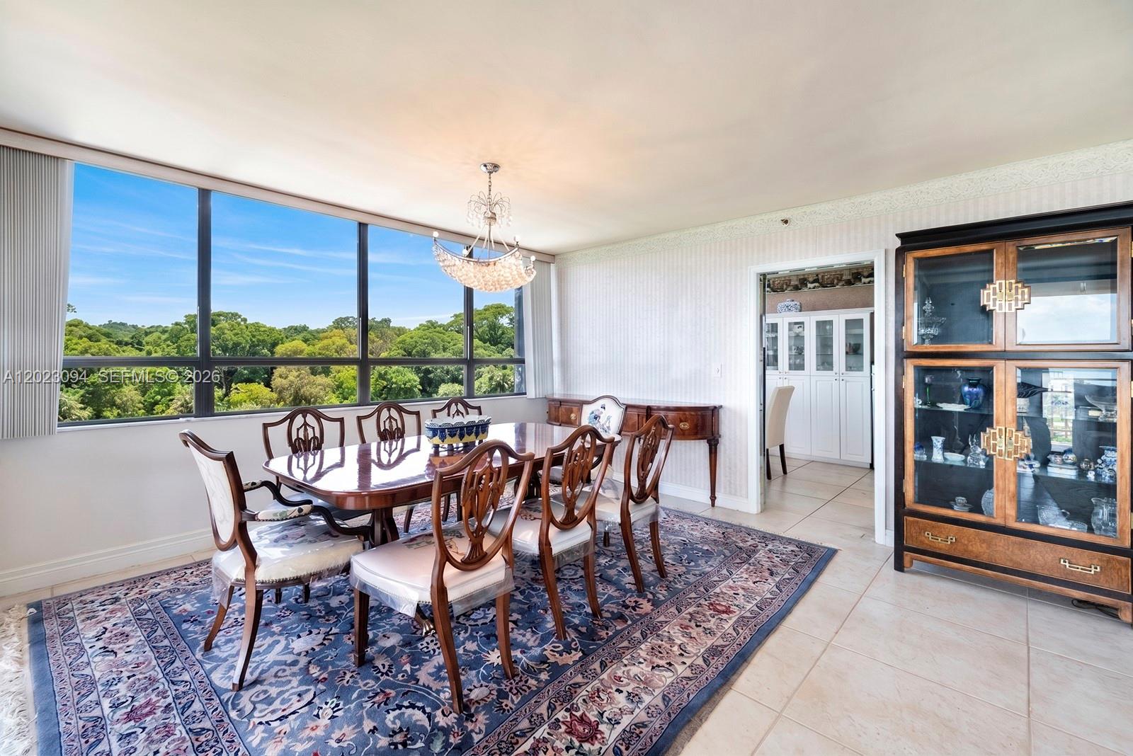A dining room with a wooden table, chairs, crystal chandelier, and large windows overlooking trees — 11113 Biscayne Blvd # 751, Miami FL 33181, MIAMI, FL