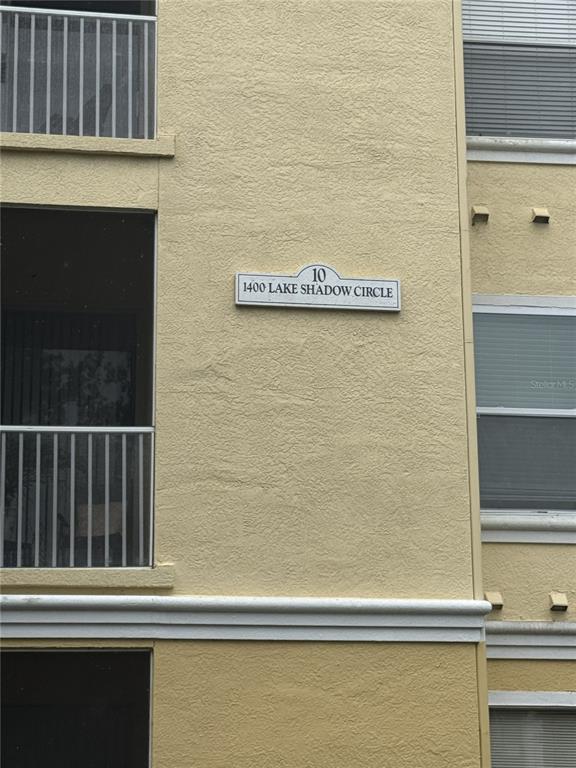 A beige stucco building exterior features a sign indicating the address and unit number — 1400 LAKE SHADOW CIRCLE UNIT 10103, MAITLAND, FL