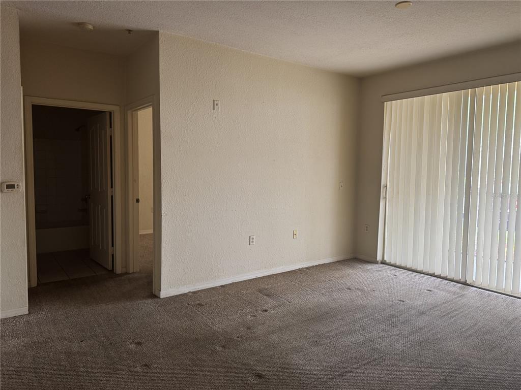 An empty room features beige carpet, textured walls, and a sliding glass door with blinds — 1400 LAKE SHADOW CIRCLE UNIT 10103, MAITLAND, FL