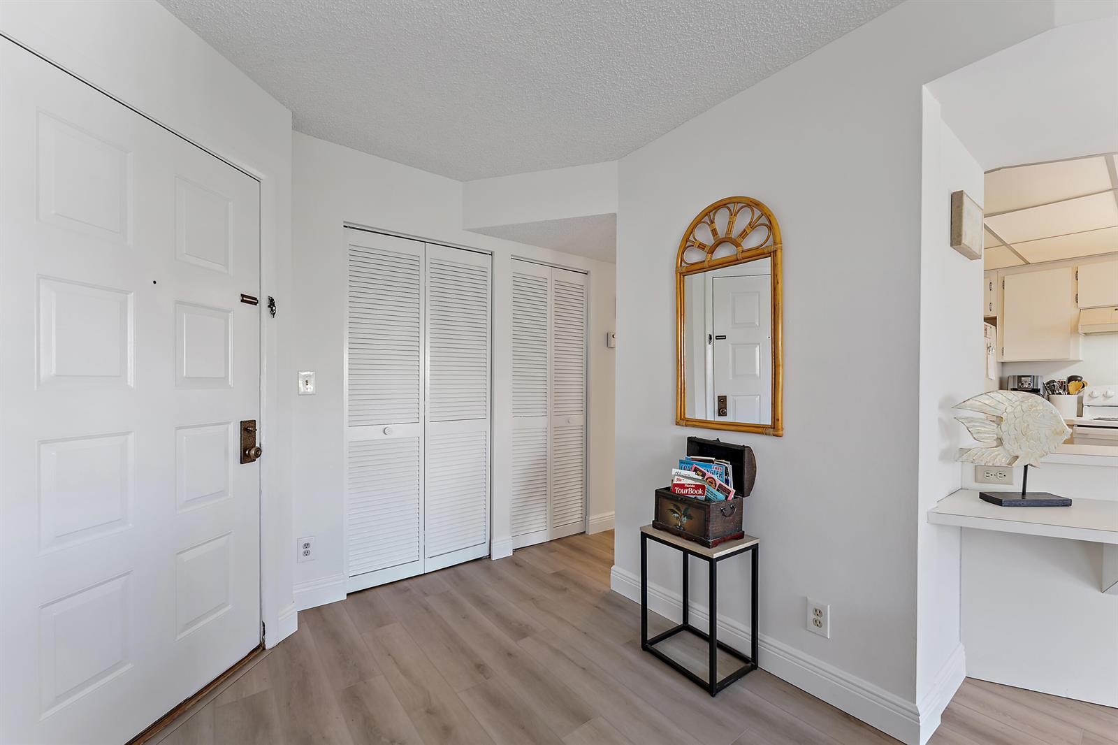 An entryway features light wood-look flooring, white louvered closet doors, and a decorative wall mirror — 1605 S Us Highway 1 # B201, Jupiter FL 33477, JUPITER, FL