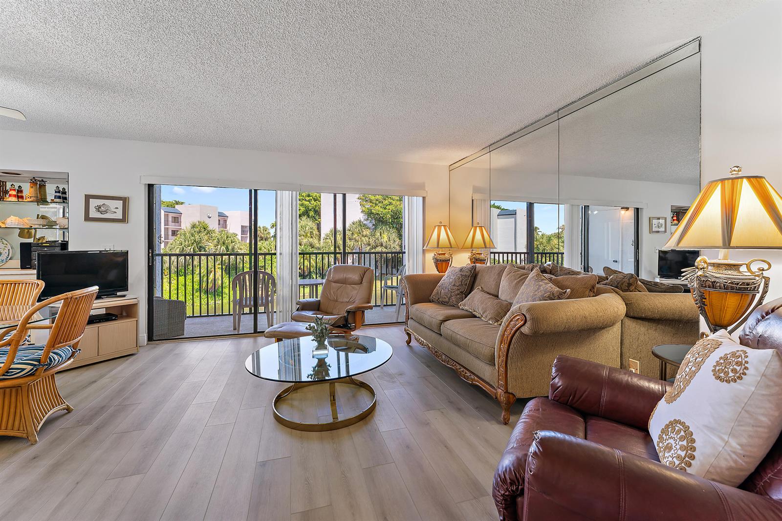 A living room features wood-look flooring, a beige sofa, leather armchairs, and a mirrored wall — 1605 S Us Highway 1 # B201, Jupiter FL 33477, JUPITER, FL