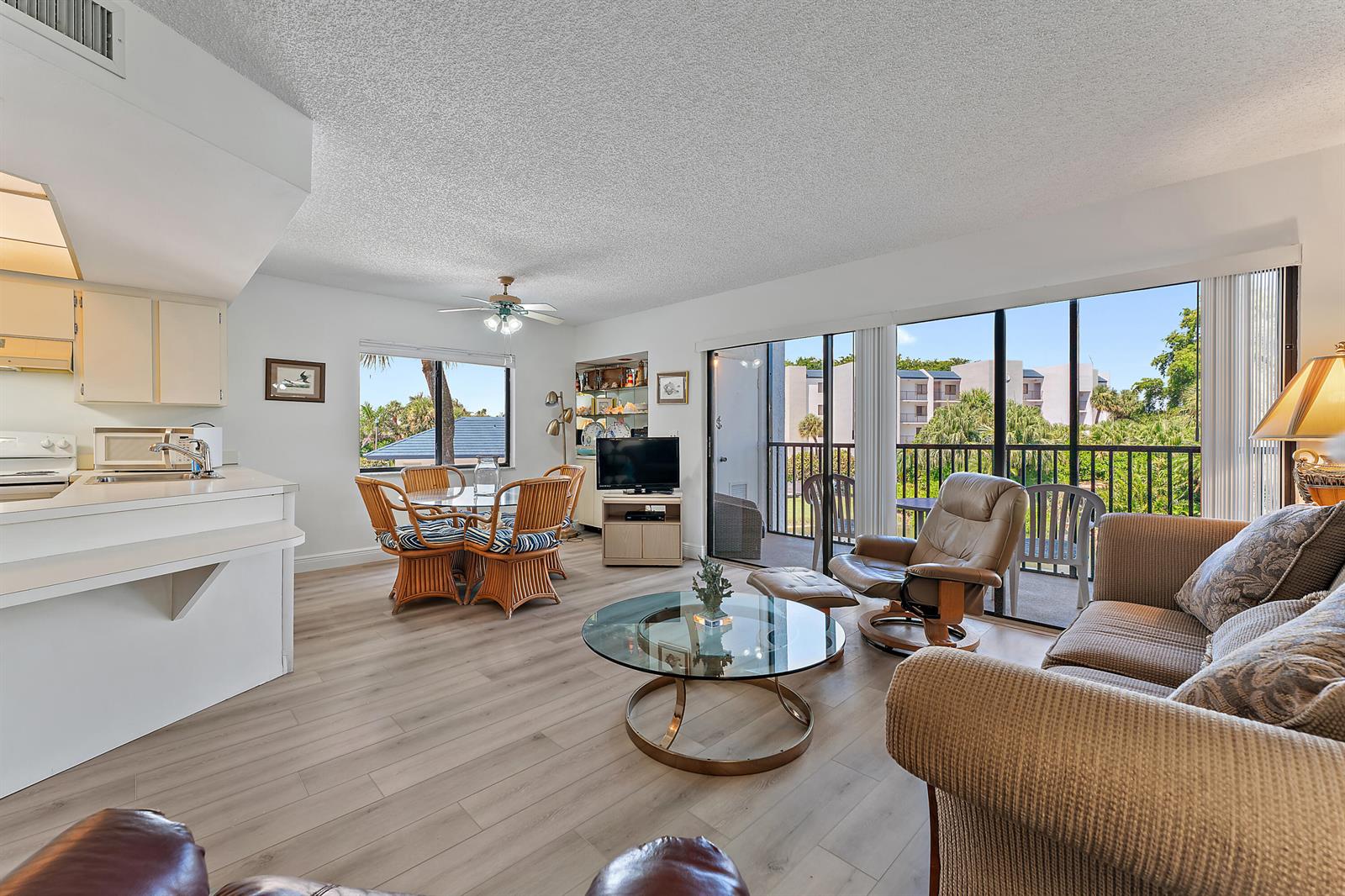 A living room and dining area with light wood floors, rattan furniture, and a balcony — 1605 S Us Highway 1 # B201, Jupiter FL 33477, JUPITER, FL