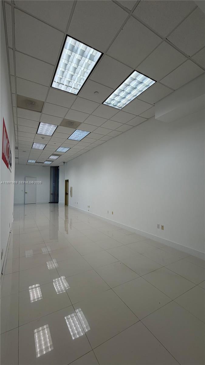 An empty, narrow office space features white walls, tiled floors, and recessed ceiling lights — 1200 Brickell Ave, Miami FL 33131, MIAMI, FL