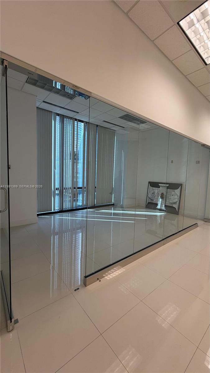 A modern office space features glass walls, white tile flooring, and vertical window blinds — 1200 Brickell Ave, Miami FL 33131, MIAMI, FL