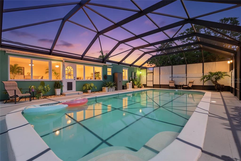 A swimming pool enclosed by a screened lanai sits beside a green house at sunset — 2900 PARK STREET N, ST PETERSBURG, FL
