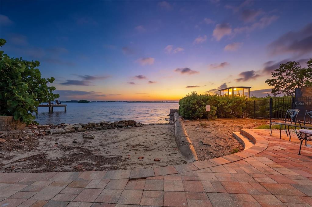 A brick patio overlooks a sandy shoreline, a small dock, and a sunset over water — 2900 PARK STREET N, ST PETERSBURG, FL