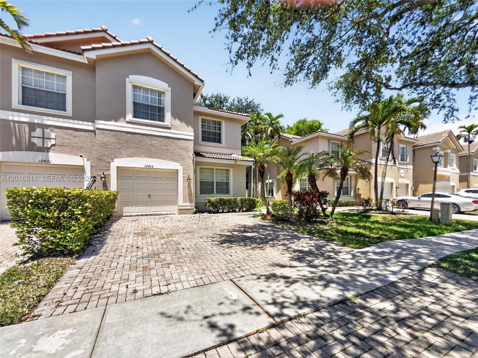 A two-story townhouse with a beige stucco exterior, a paved driveway, and palm trees — 12415 SW 42nd St, Miramar FL 33027, MIRAMAR, FL
