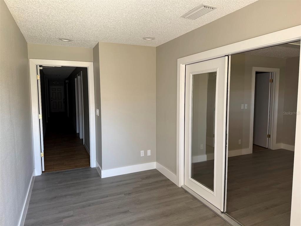 A room with gray wood-look flooring, a hallway entrance, and a glass-paneled sliding door — 2801 SW COLLEGE ROAD UNIT 22, OCALA, FL