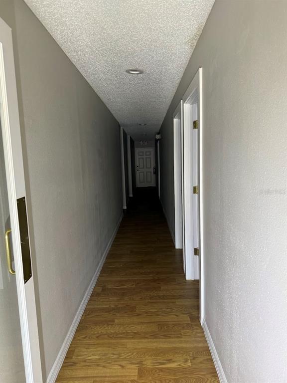 A narrow hallway with light-colored walls, wood-look flooring, and a textured ceiling — 2801 SW COLLEGE ROAD UNIT 22, OCALA, FL