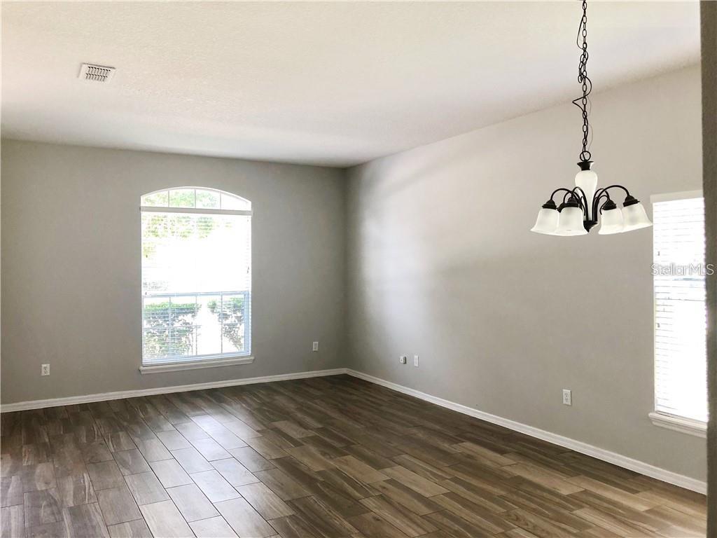 An empty room features gray walls, wood-look flooring, a chandelier, and two windows — 112 BELGIAN WAY, SANFORD, FL
