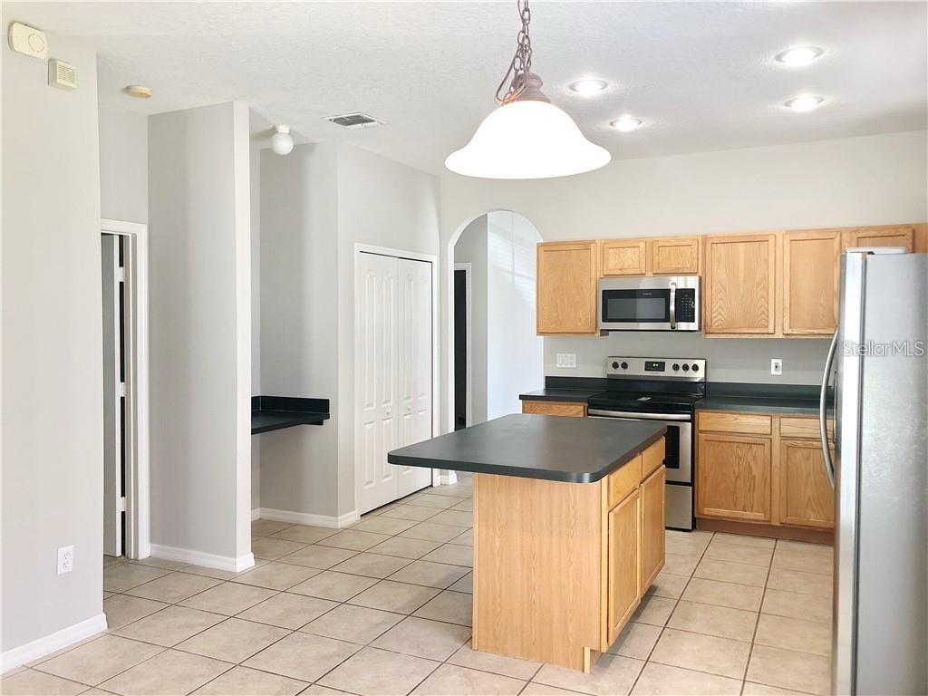 A kitchen features light wood cabinets, a black island, stainless steel appliances, and tile flooring — 112 BELGIAN WAY, SANFORD, FL