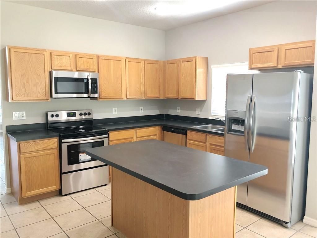 A kitchen features light wood cabinets, stainless steel appliances, a center island, and dark countertops — 112 BELGIAN WAY, SANFORD, FL