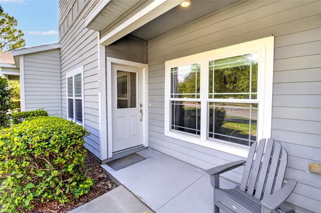 A gray-sided home exterior features a front porch, a white door, and a wooden chair — 5008 NW 21ST DRIVE, GAINESVILLE, FL
