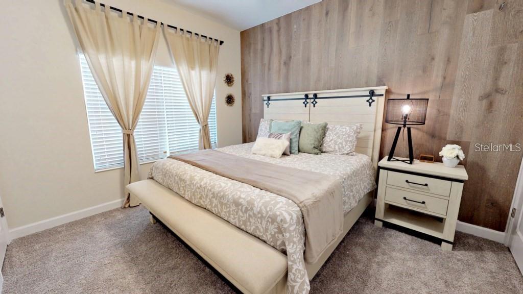 A bedroom features a king bed with a wood-paneled accent wall and beige curtains — 4966 WINDERMERE AVENUE, KISSIMMEE, FL