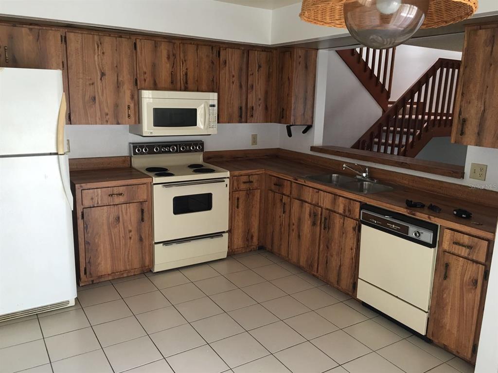 A kitchen features wood-grain cabinets, white appliances, tile flooring, and a view of stairs — 4416 RING NECK ROAD UNIT 18B, ORLANDO, FL