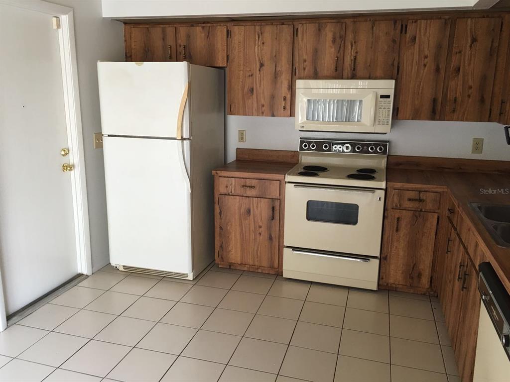 A kitchen with wood cabinets, white appliances, and light-colored floor tiles — 4416 RING NECK ROAD UNIT 18B, ORLANDO, FL